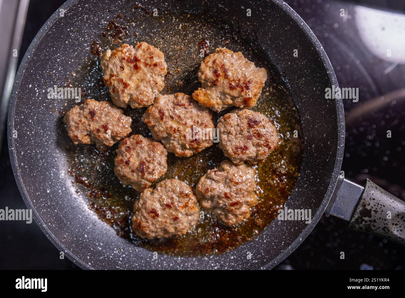 Polpettine di hamburger perfettamente scottate in una padella, dorate e pronte per essere servite, sedute in un saporito olio. Foto Stock