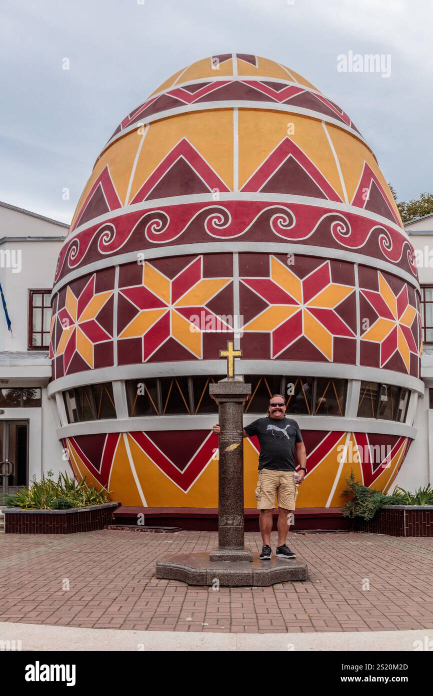 Un uomo si trova di fronte a un grande e colorato edificio a forma di uovo. L'edificio è decorato con motivi rossi, gialli e bianchi ed è una chiesa o. Foto Stock