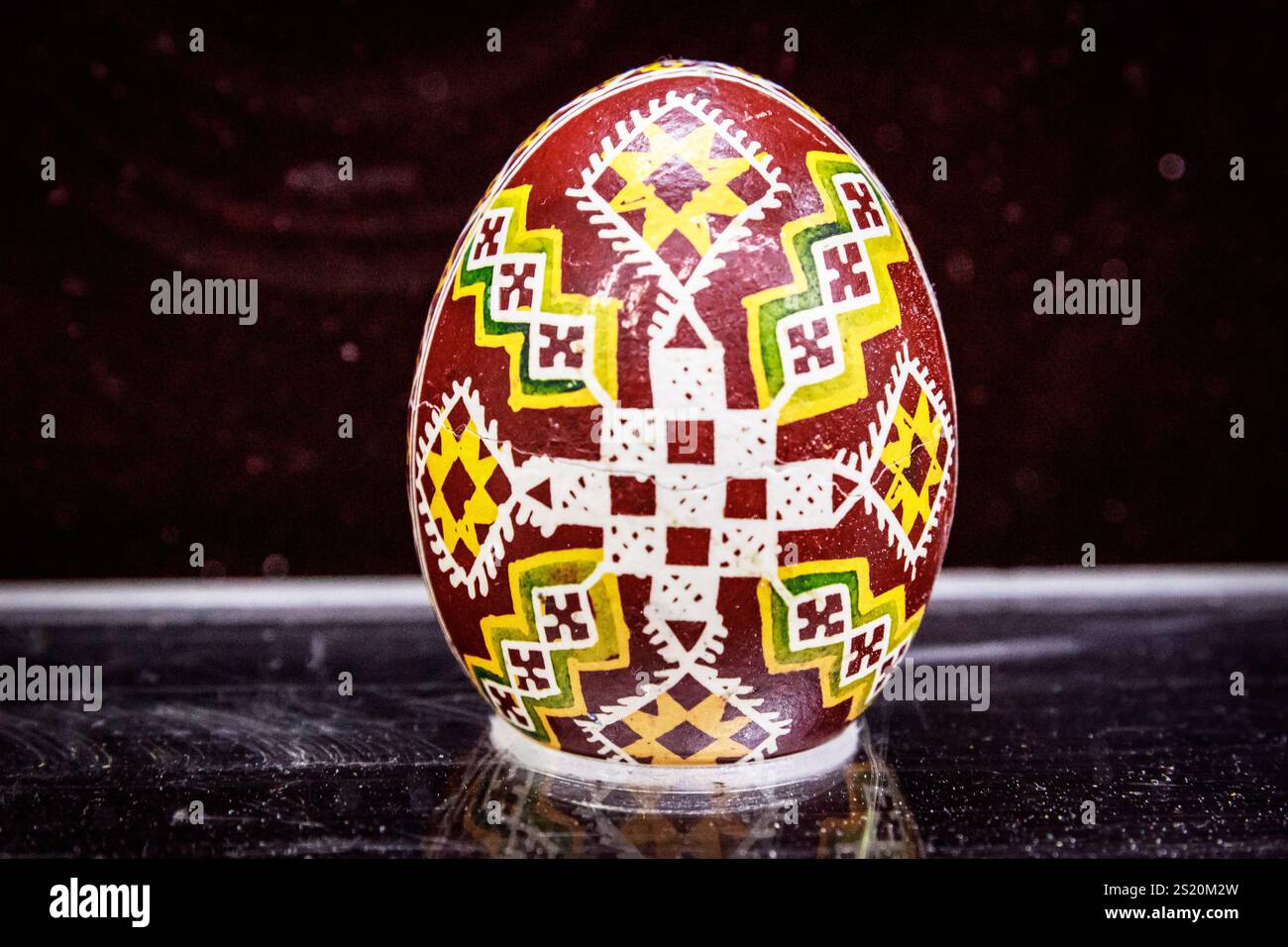 Un uovo colorato con disegno a croce si trova su un tavolo. L'uovo è decorato con motivi e colori intricati, rendendolo un pezzo bello e unico Foto Stock