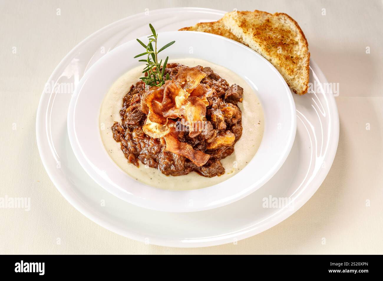Un piatto di cibo con un pezzo di pane sul lato. Il cibo è uno stufato con carne e verdure Foto Stock