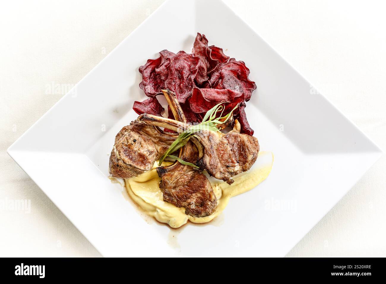 Un piatto di costolette di agnello con un lato di patate e una salsa. La piastra è bianca e rettangolare Foto Stock