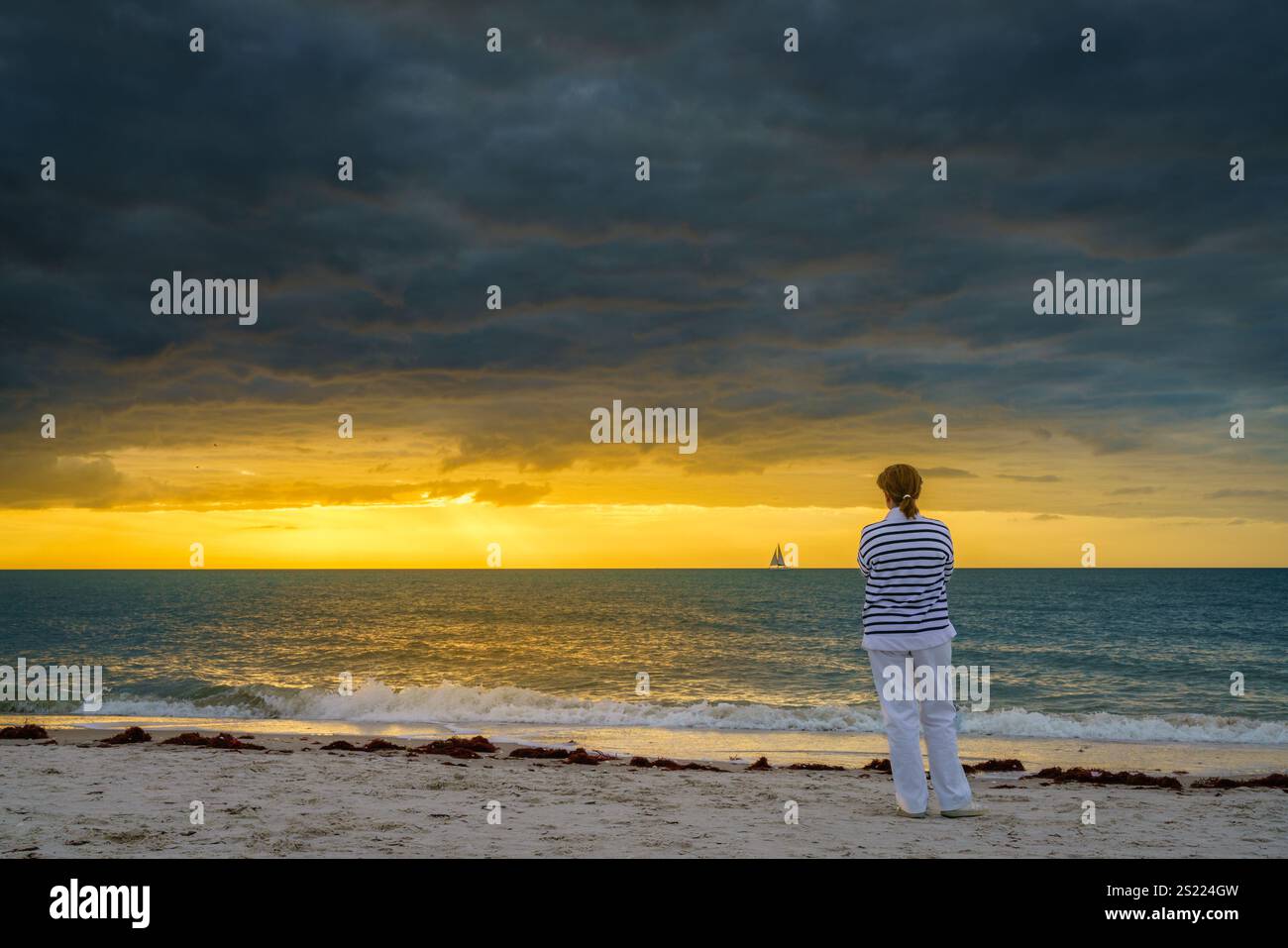 Una donna sta guardando il tramonto sulla spiaggia di Naples, Florida Foto Stock