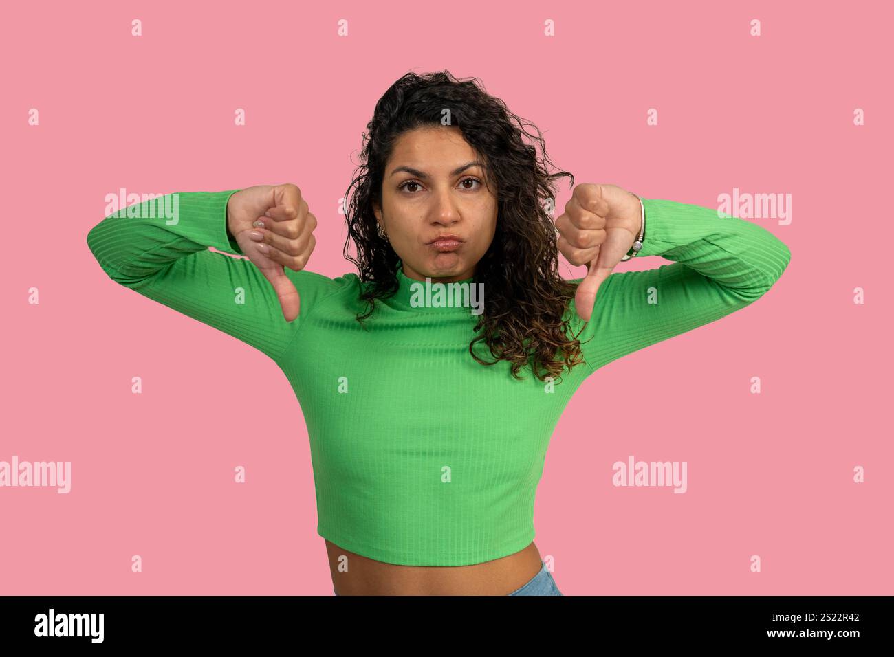 Giovane donna che mostra un gesto con il pollice verso il basso che esprime disprezzo, disapprovazione, disaccordo o feedback negativo su sfondo rosa Foto Stock