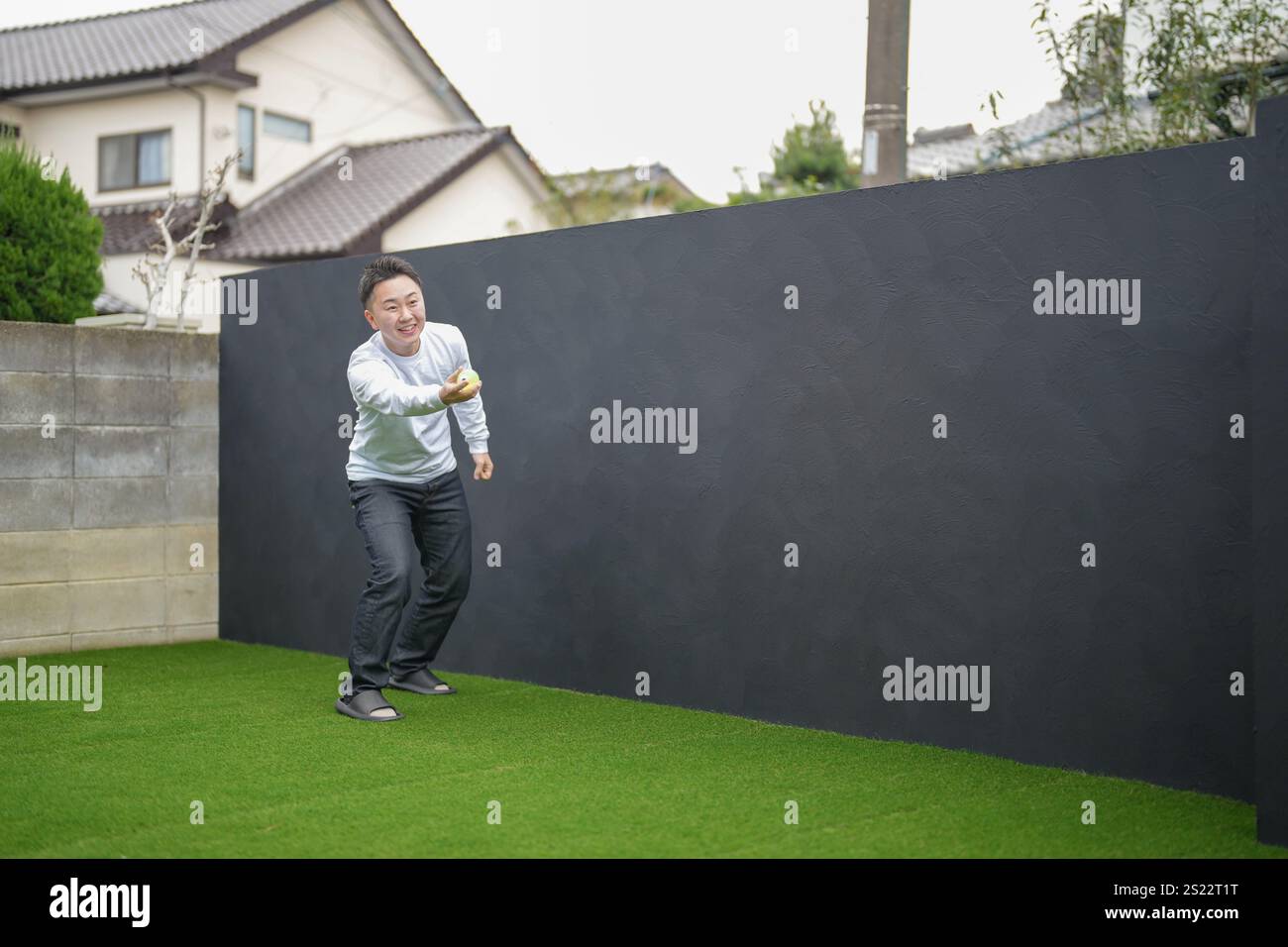 Un genitore e un bambino giapponesi, un uomo di 20 anni e una bambina di 6 anni, giocano lanciando palle di plastica verdi l'uno contro l'altro nel giardino recintato di Foto Stock
