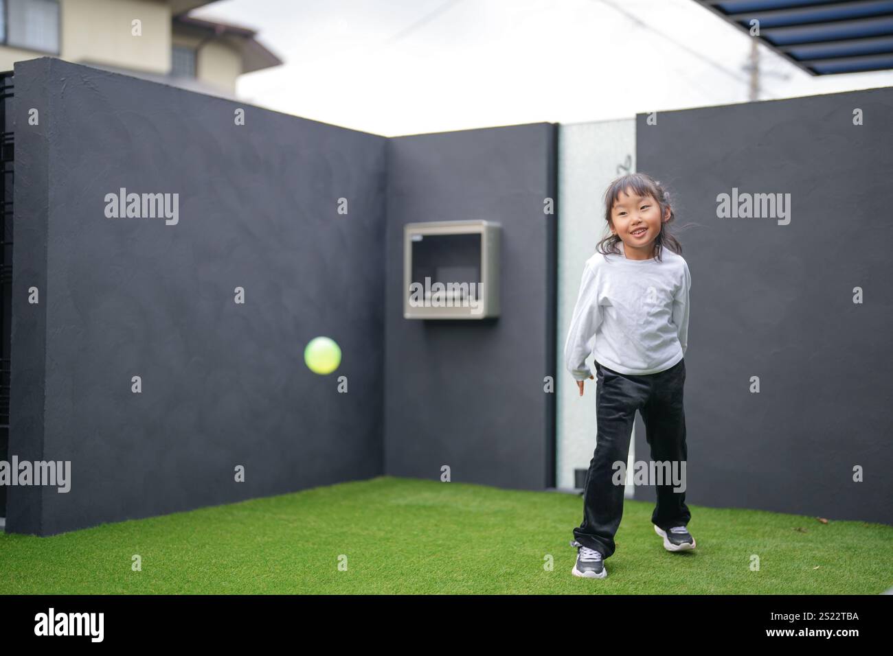 Un genitore e un bambino giapponesi, un uomo di 20 anni e una bambina di 6 anni, giocano lanciando palle di plastica verdi l'uno contro l'altro nel giardino recintato di Foto Stock