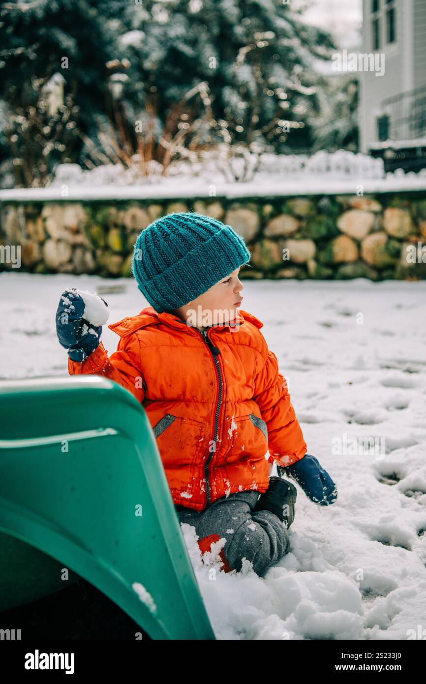 Bambino che tiene la palla di neve su uno scivolo verde Foto Stock