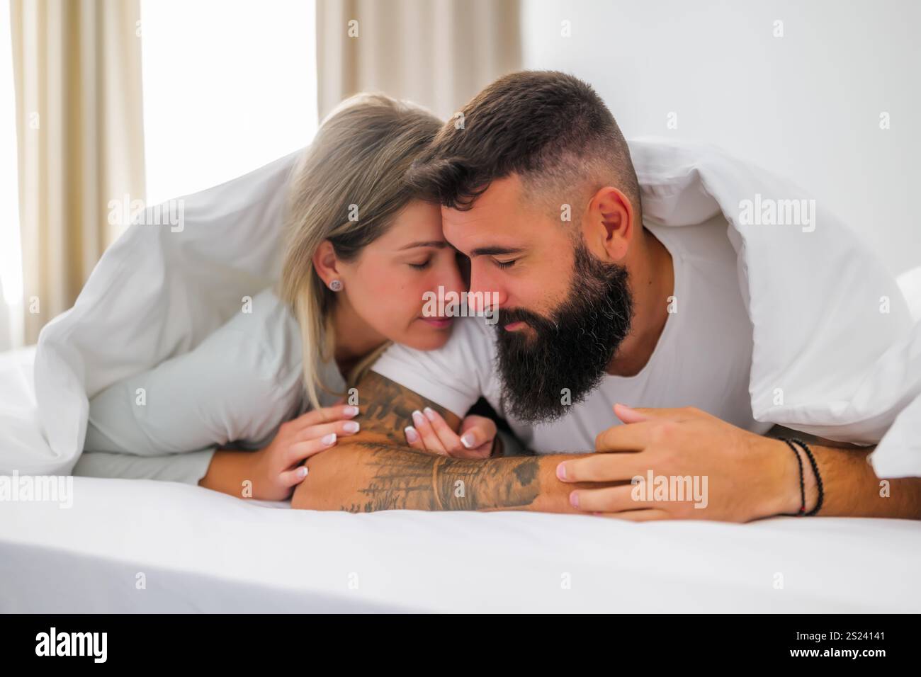 La mattina, una giovane coppia felice e amorevole è sdraiata a letto. Stanno abbracciando. Foto Stock