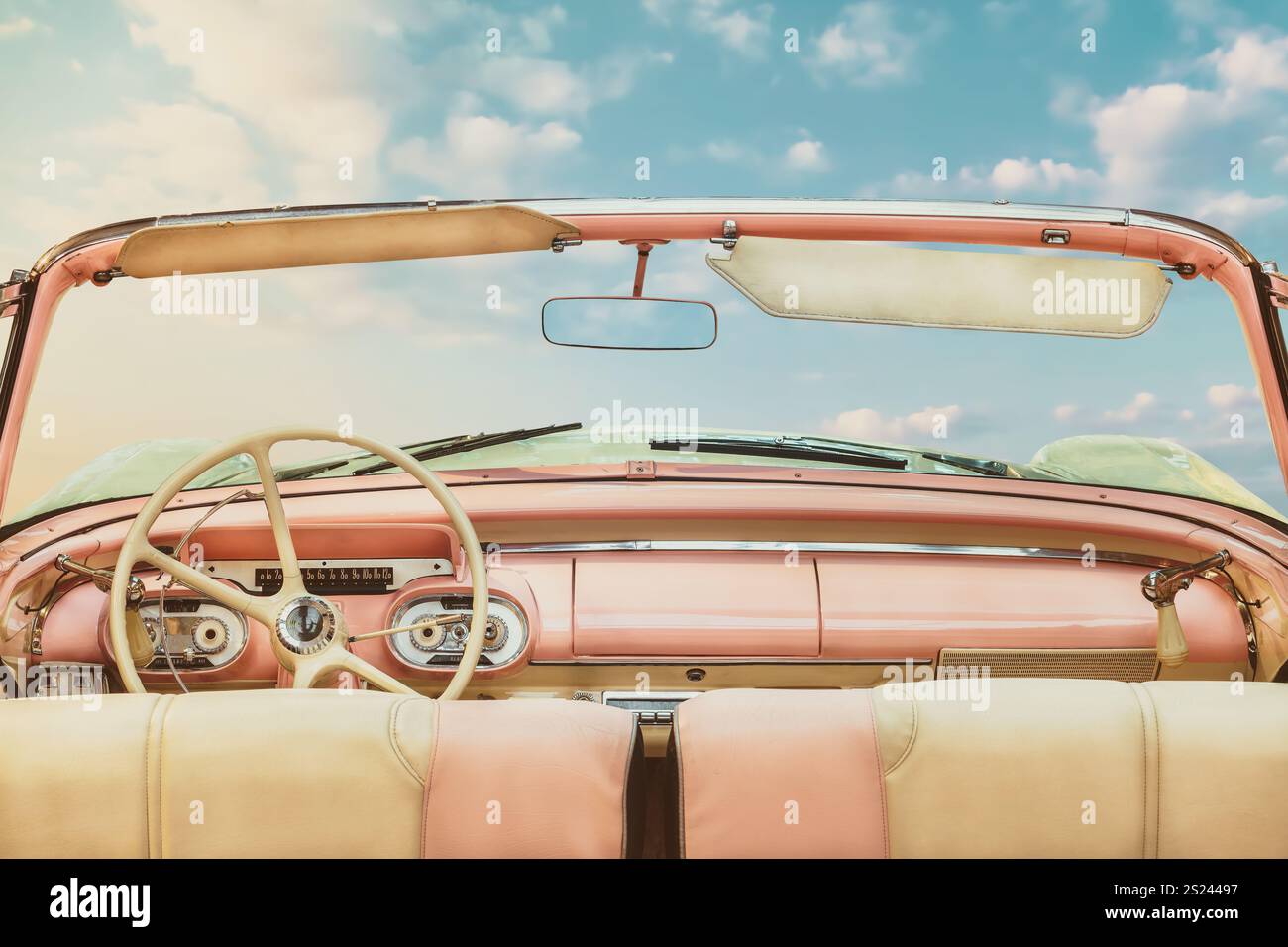 Vista del conducente di una classica cabriolet americana aperta rosa d'epoca di fronte a un cielo azzurro soleggiato Foto Stock