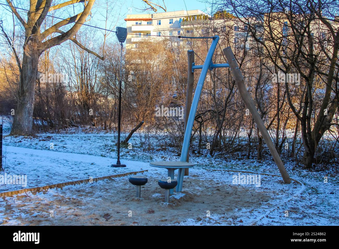 Un'altalena e un'area salotto circolare sorgono in un parco innevato circondato da alberi e dalla luce del sole in inverno. Foto Stock