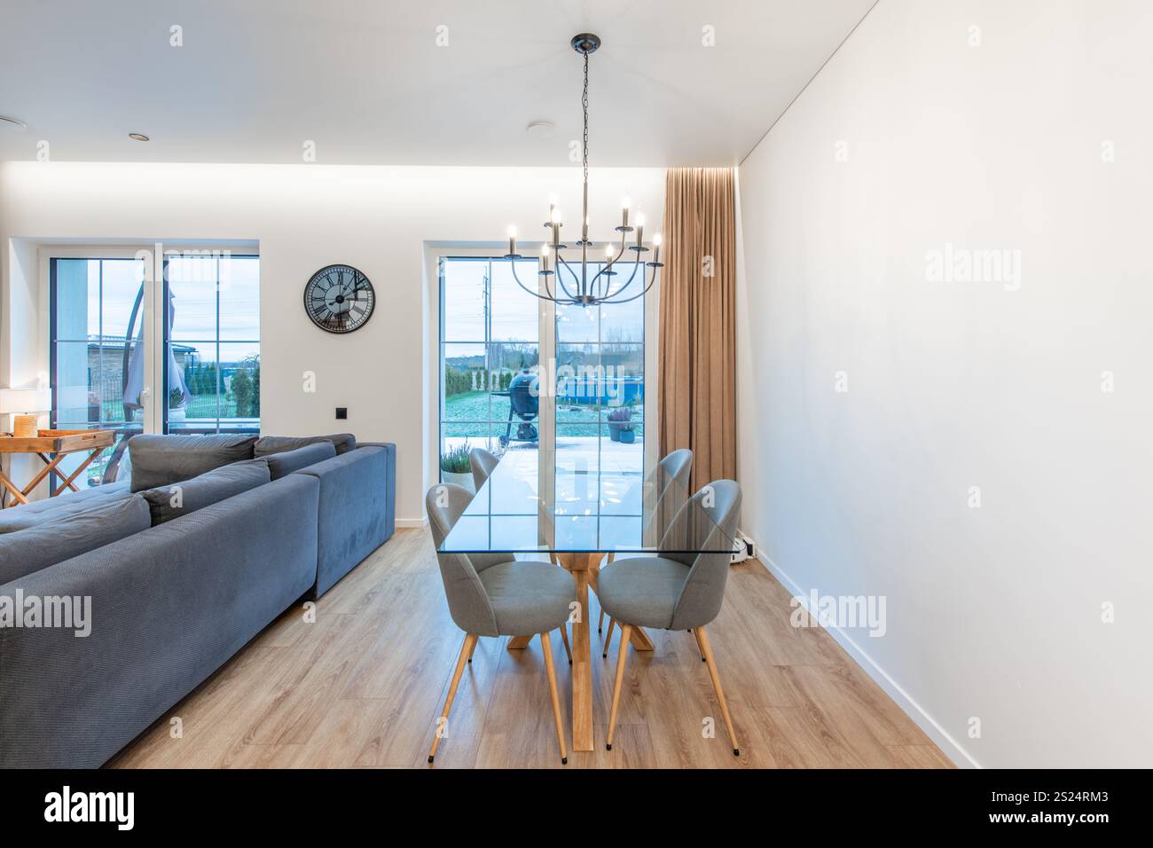 Soggiorno contemporaneo con pavimenti in legno duro, arredi eleganti e tavolo da pranzo in vetro, completato dalla luce naturale dalle grandi finestre. Ideale Foto Stock