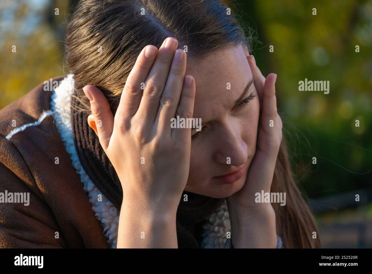 Ritratto di una donna triste con mal di testa, che tiene le mani ai templi nel parco, sentendosi malata e stanca in autunno Foto Stock