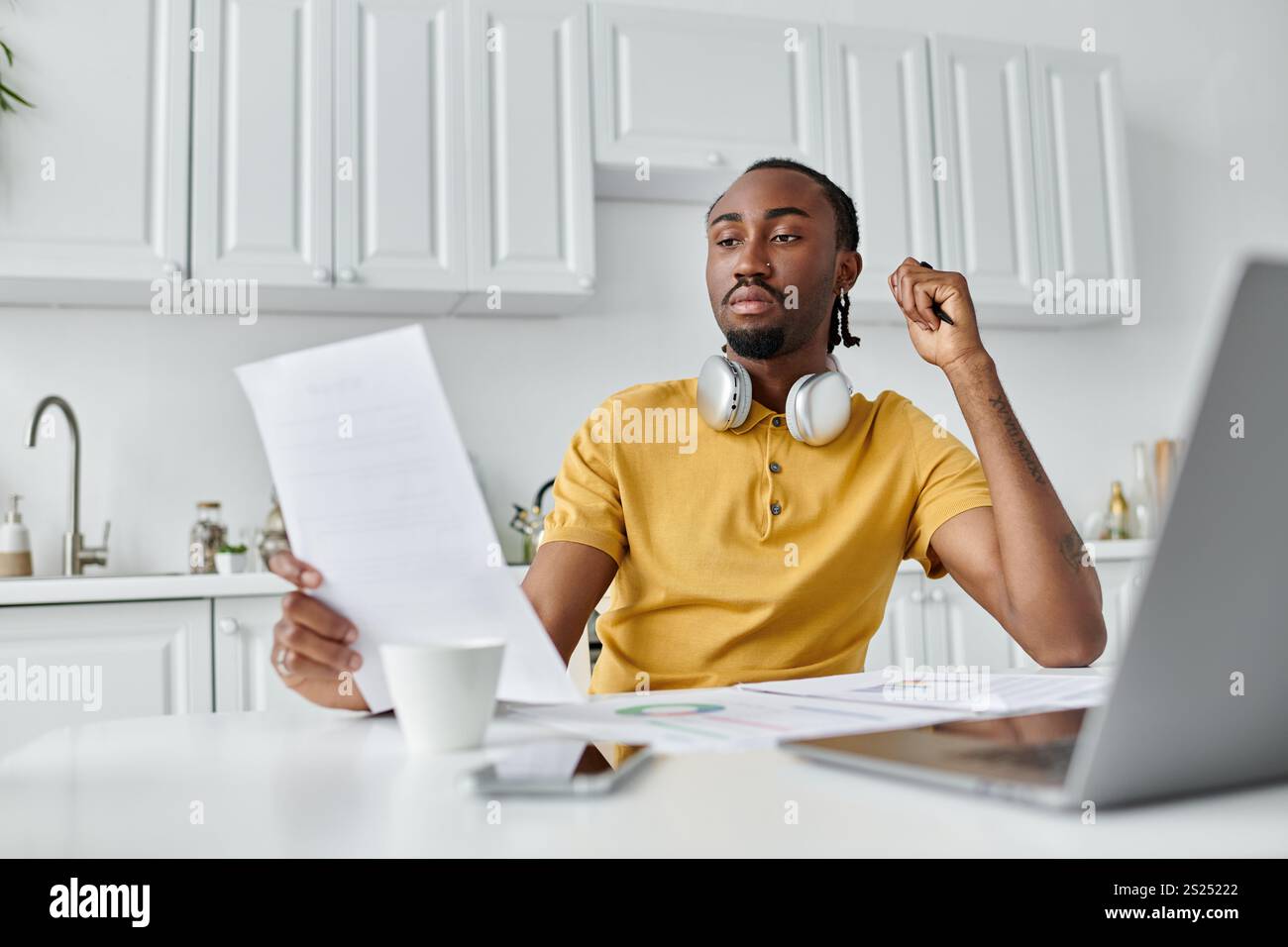 Un giovane attento esamina i documenti in una cucina elegante, immersa nel suo lavoro remoto. Foto Stock