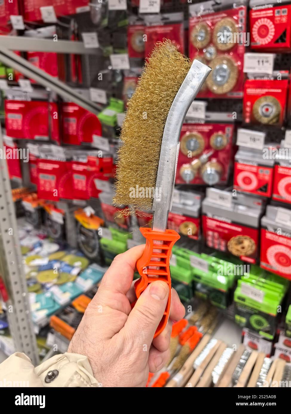 Una mano tiene una spazzola per la pulizia dal design esclusivo in un negozio di ferramenta ben fornito, circondato da confezioni colorate e vari strumenti, creando un mezzo di vita Foto Stock