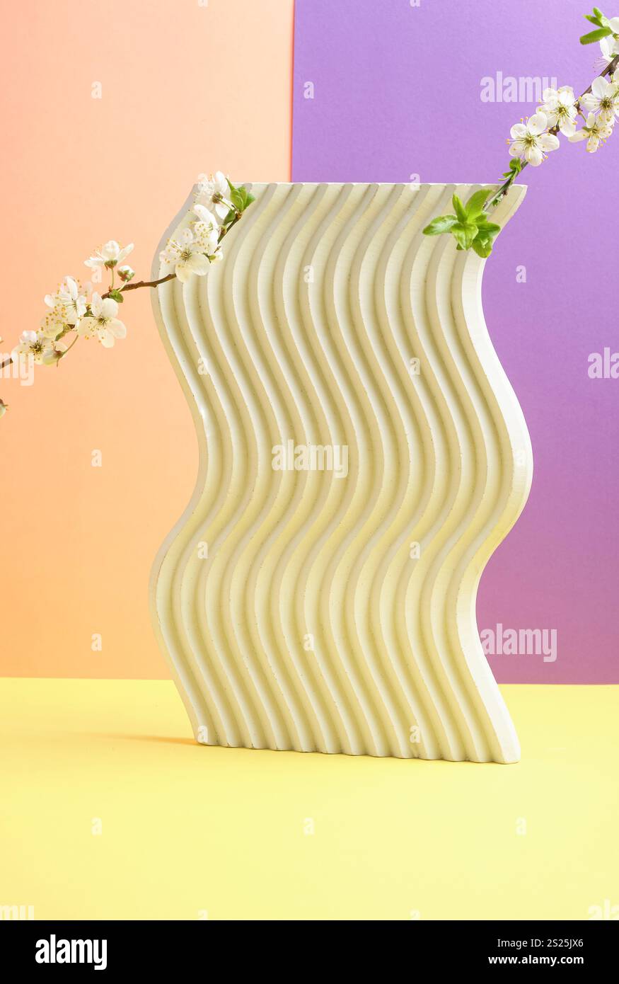 Composizione minimalista caratterizzata da un supporto in cemento ondulato con rami in fiore disposti artisticamente, su un vibrante giallo arancione Foto Stock