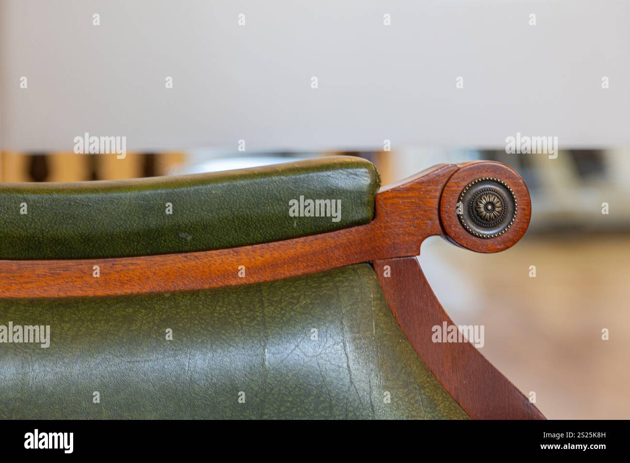 Una vista ravvicinata di un'elegante sedia in pelle verde che presenta un bracciolo in legno dal design splendido. La sedia è collocata in un ambiente interno ben illuminato Foto Stock