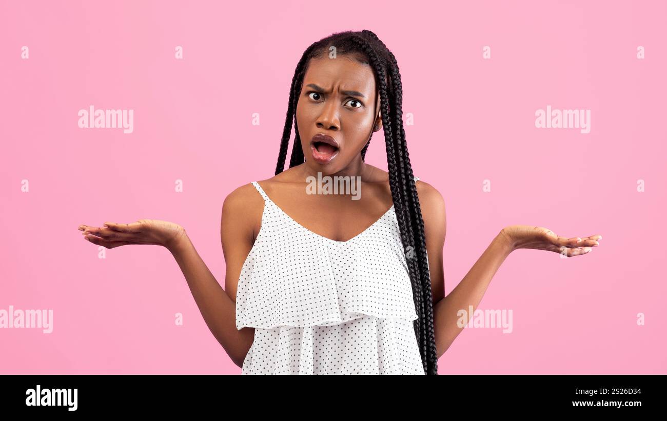 Irritata donna afroamericana che mostra un gesto che NON CONOSCO, che stringe le spalle sullo sfondo rosa dello studio Foto Stock