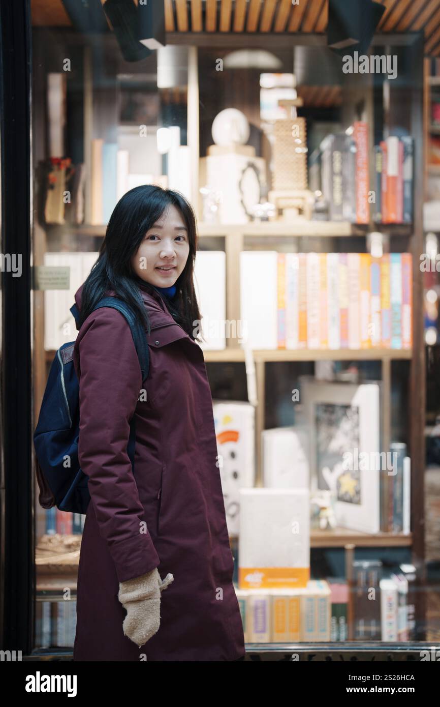 Una donna asiatica in piedi di fronte ad una libreria Foto Stock