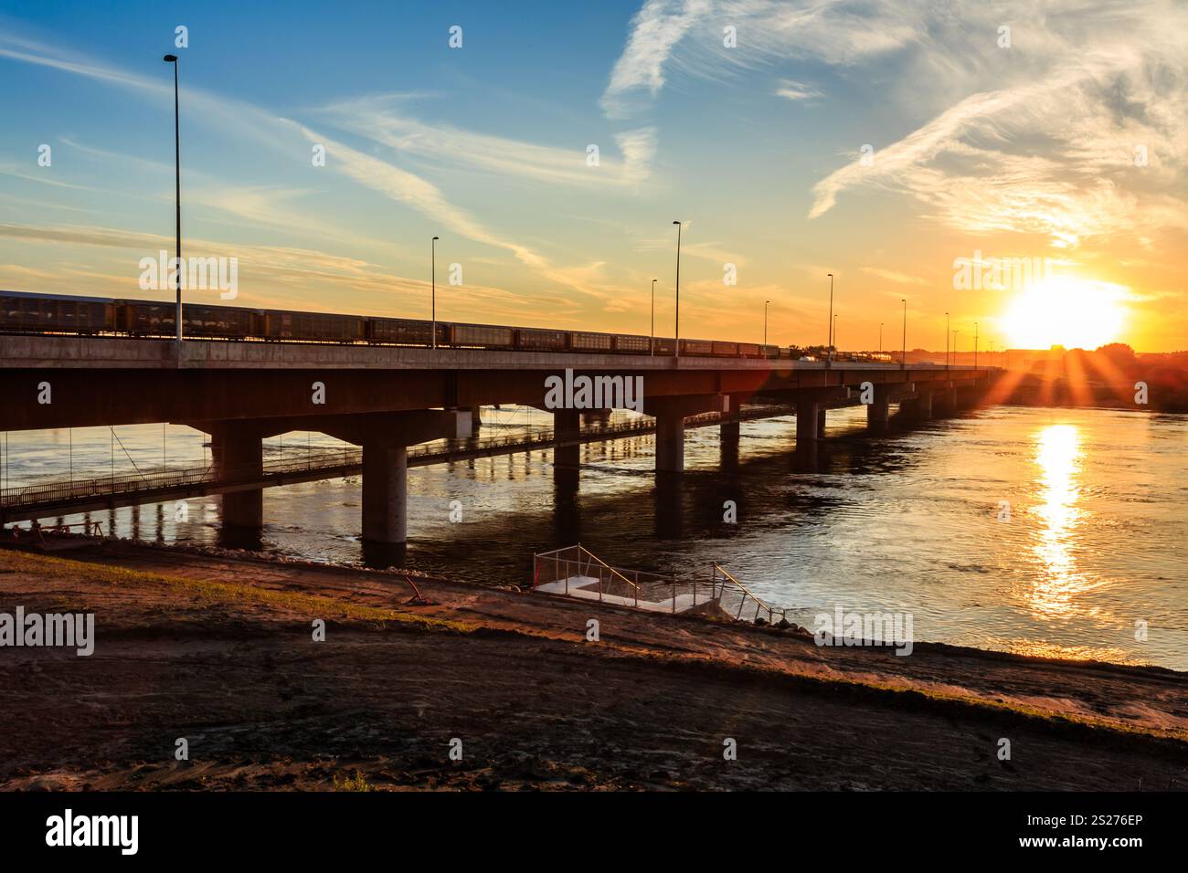 Un ponte su un fiume con un tramonto sullo sfondo. Il ponte è illuminato dal sole, creando un'atmosfera calda e tranquilla Foto Stock