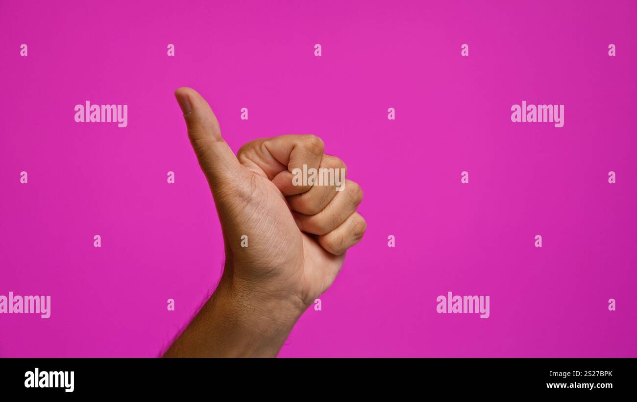 Uomo che dà un gesto con il pollice su uno sfondo rosa brillante, proiettando positività e approvazione Foto Stock