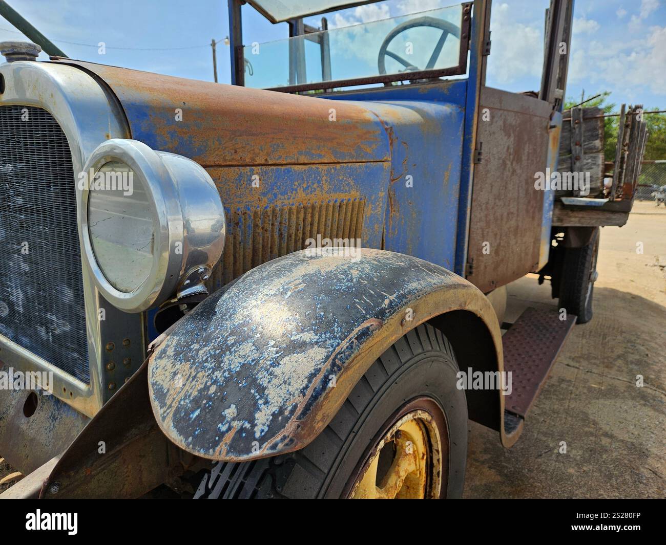 Camion arrugginito d'epoca parcheggiato su una strada sterrata sotto cieli azzurri in un ambiente all'aperto - Immagine stock catturata con smartphone