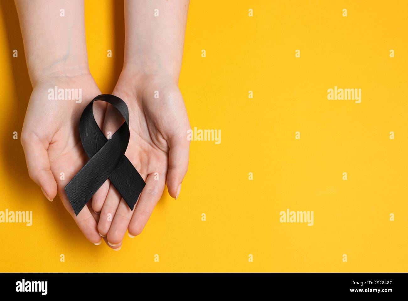 Donna con nastro nero su sfondo giallo, vista dall'alto con spazio per il testo. Concetto di melanoma e lutto Foto Stock