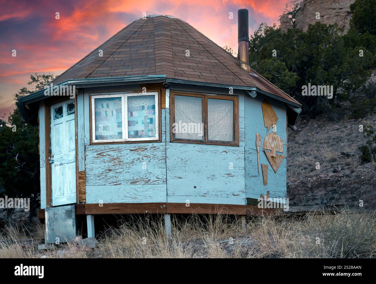 Una struttura simile a una yurta realizzata con pannelli di legno blu con tetto in tegole e camino con uno sfondo di vibranti tramonti mentre vivi fuori dalla griglia Foto Stock