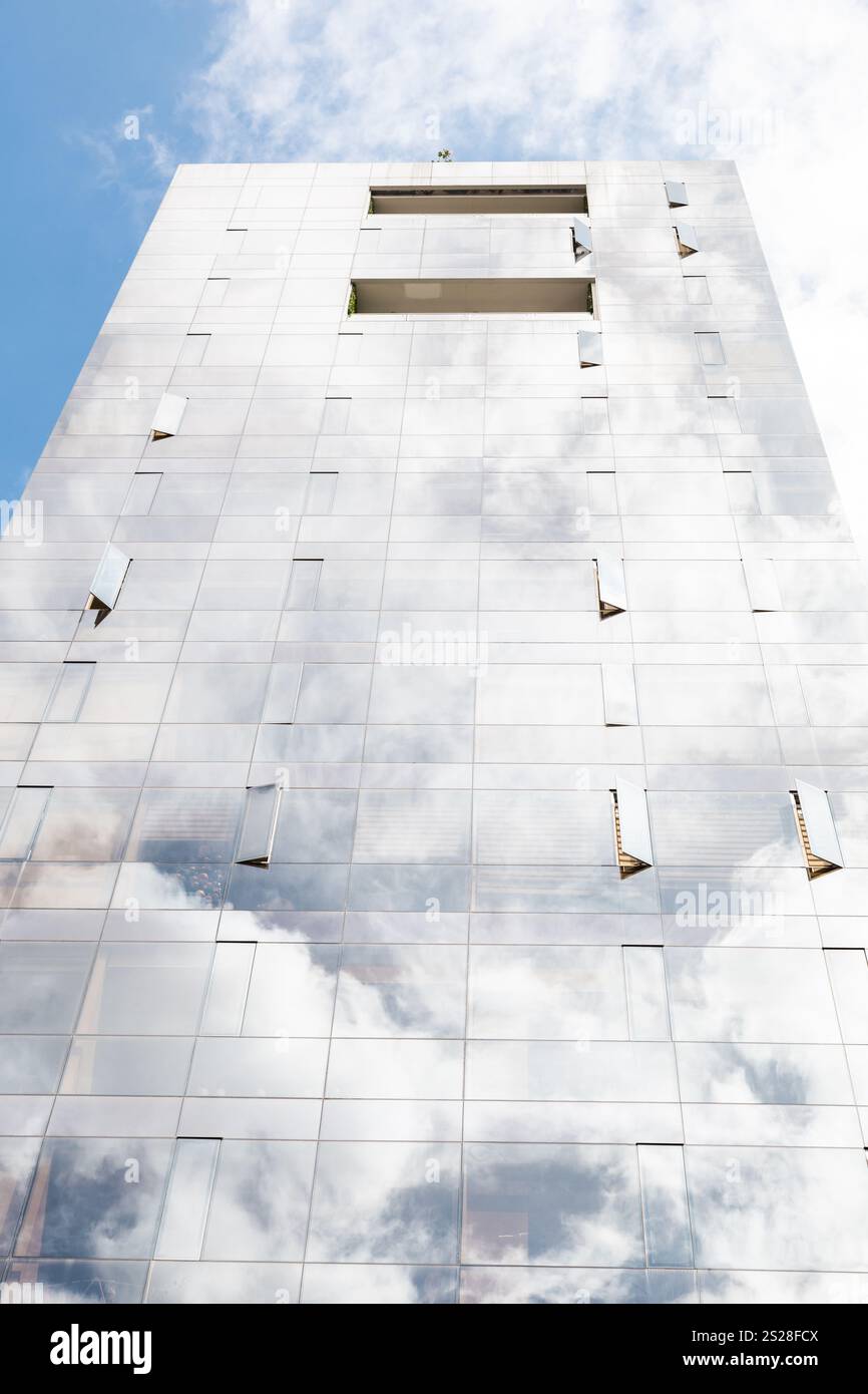 Un edificio di vetro che si fonde perfettamente con il cielo, riflettendo le nuvole e l'ambiente circostante. La sua superficie trasparente crea una straordinaria armonia visiva, Foto Stock