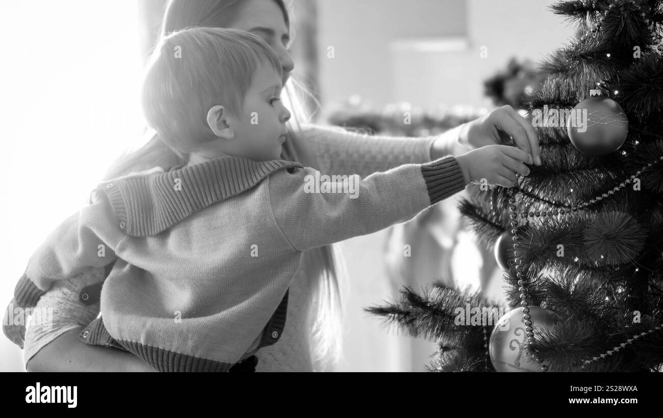 Immagine in bianco e nero di un bambino che decora l'albero di Natale con baubles Foto Stock