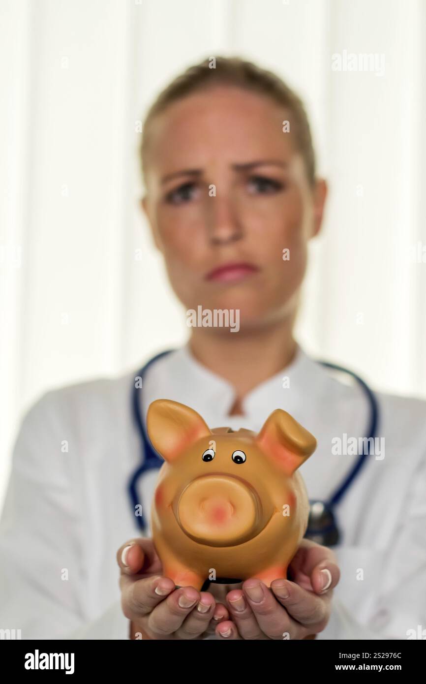 Un giovane medico ha in mano un salvadanaio. Foto simbolica per le tasse del medico, apertura di uno studio e assicurazione pensionistica. Austria Foto Stock