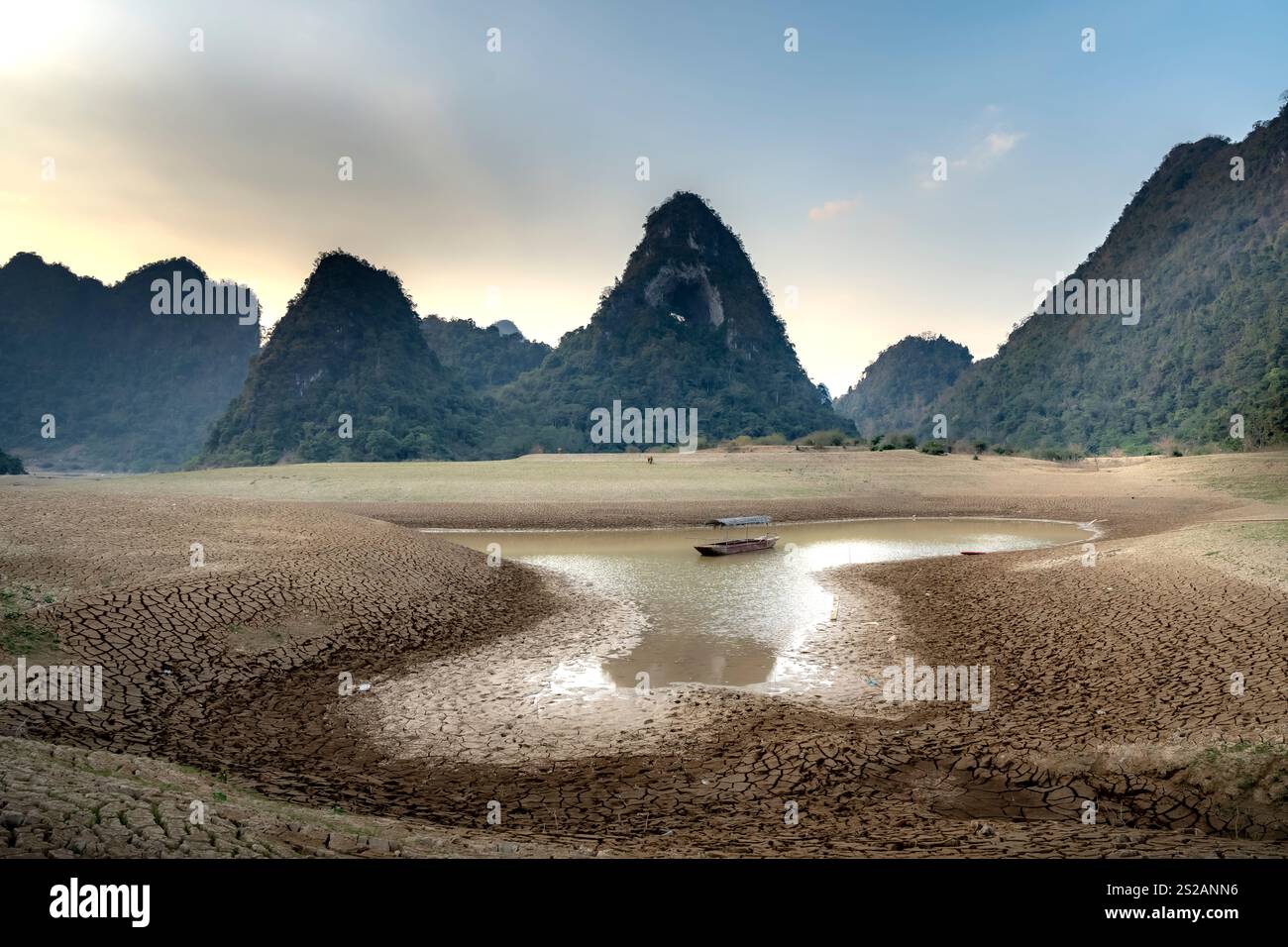 Letto di lago asciutto al tramonto, con fango incrinato sul fondo del lago, cielo blu, nuvole e montagne nella provincia di Cao Bang, Vietnam Foto Stock