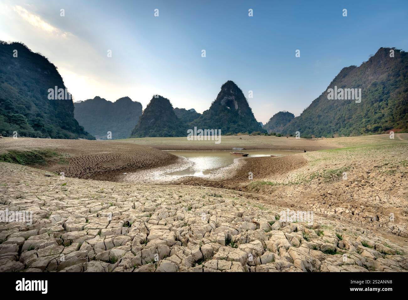 Letto di lago asciutto al tramonto, con fango incrinato sul fondo del lago, cielo blu, nuvole e montagne nella provincia di Cao Bang, Vietnam Foto Stock