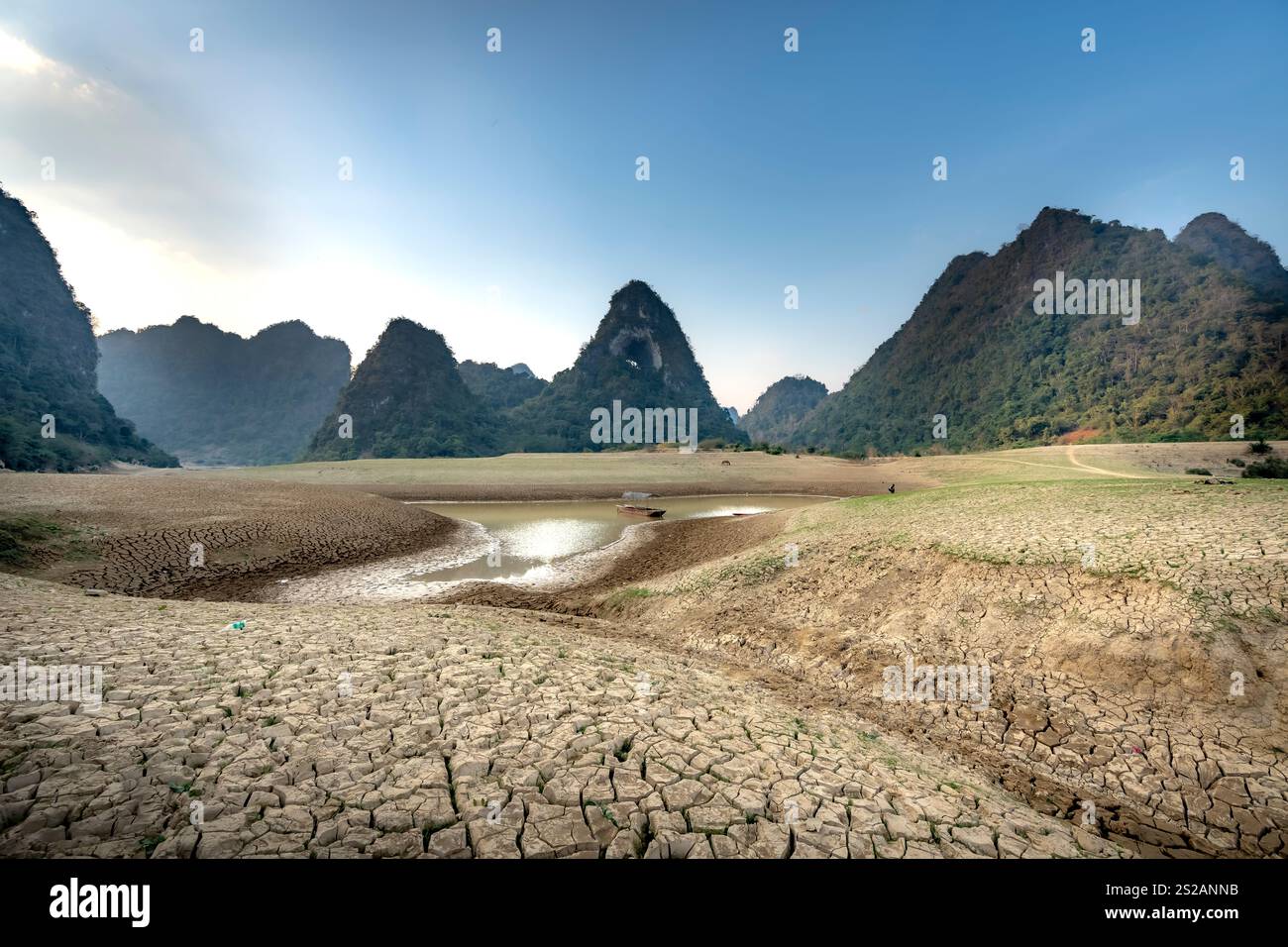Letto di lago asciutto al tramonto, con fango incrinato sul fondo del lago, cielo blu, nuvole e montagne nella provincia di Cao Bang, Vietnam Foto Stock