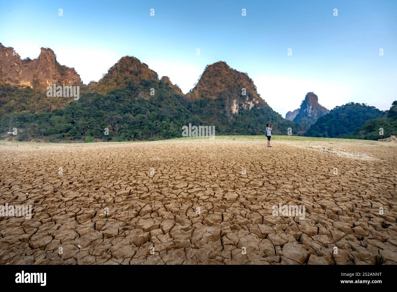 Letto di lago asciutto al tramonto, con fango incrinato sul fondo del lago, cielo blu, nuvole e montagne nella provincia di Cao Bang, Vietnam Foto Stock