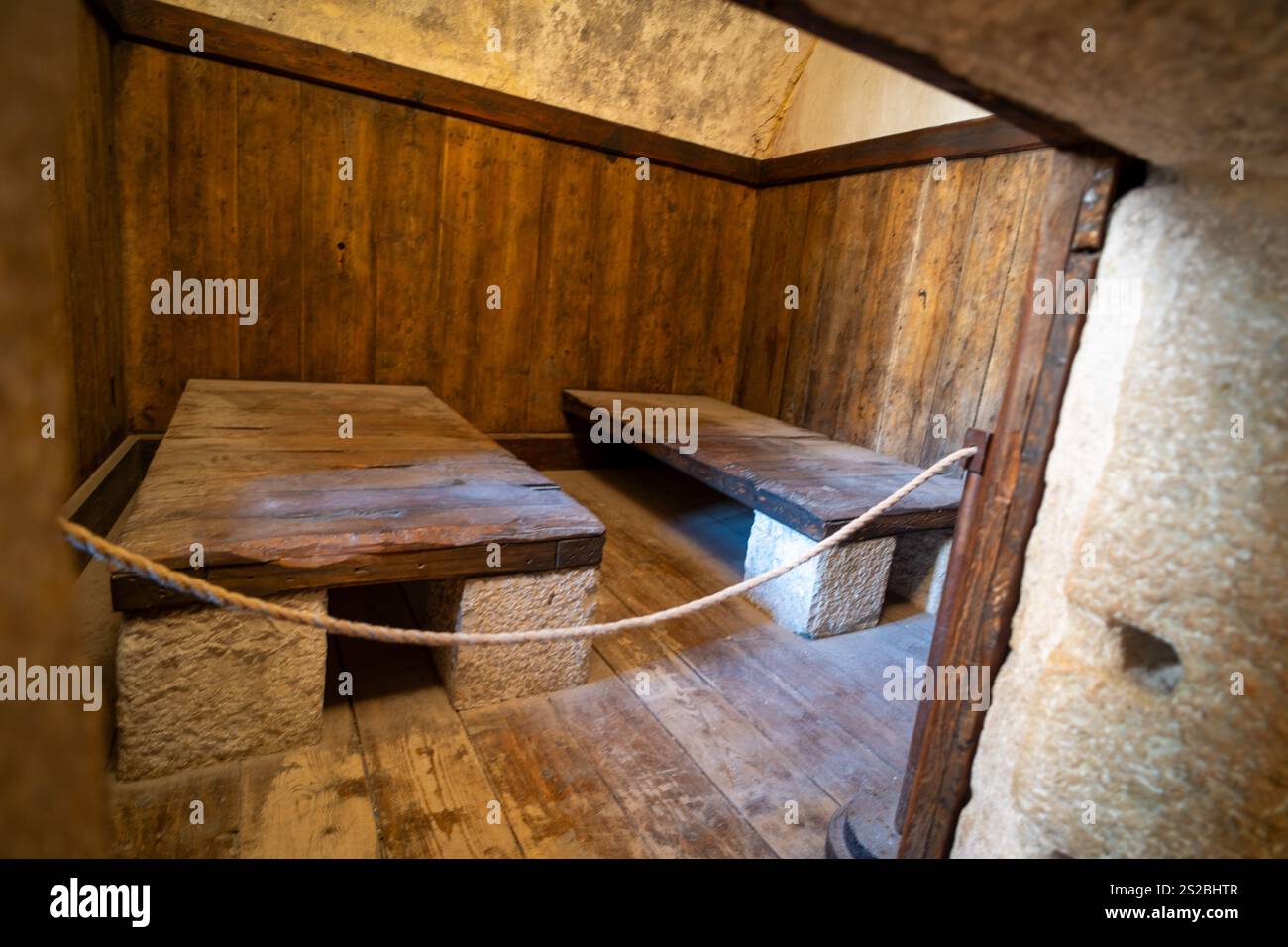 Una piccola cella storica, poco illuminata, caratterizzata da pareti in legno, supporti in pietra e due semplici letti in legno, separati da una barriera di corda. Foto Stock