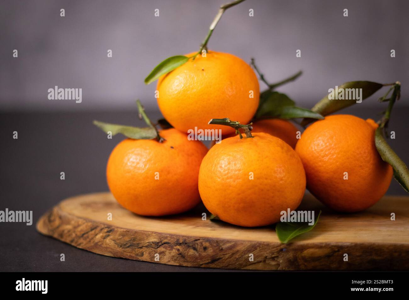 Un mucchio di frutti mandarini interi con foglie su piatto di legno, sfondo grigio del tavolo Foto Stock