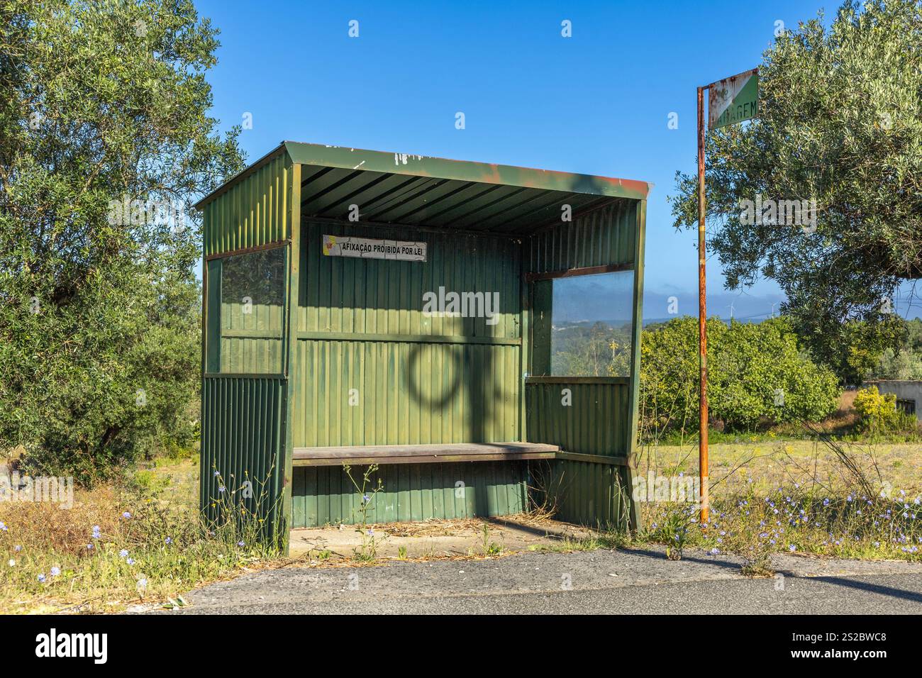 Stazione degli autobus verde in alluminio con panca in legno in Portogallo con un cartello arrugginito fermata 'Paragem' in un villaggio 'Vila do Paco' Foto Stock