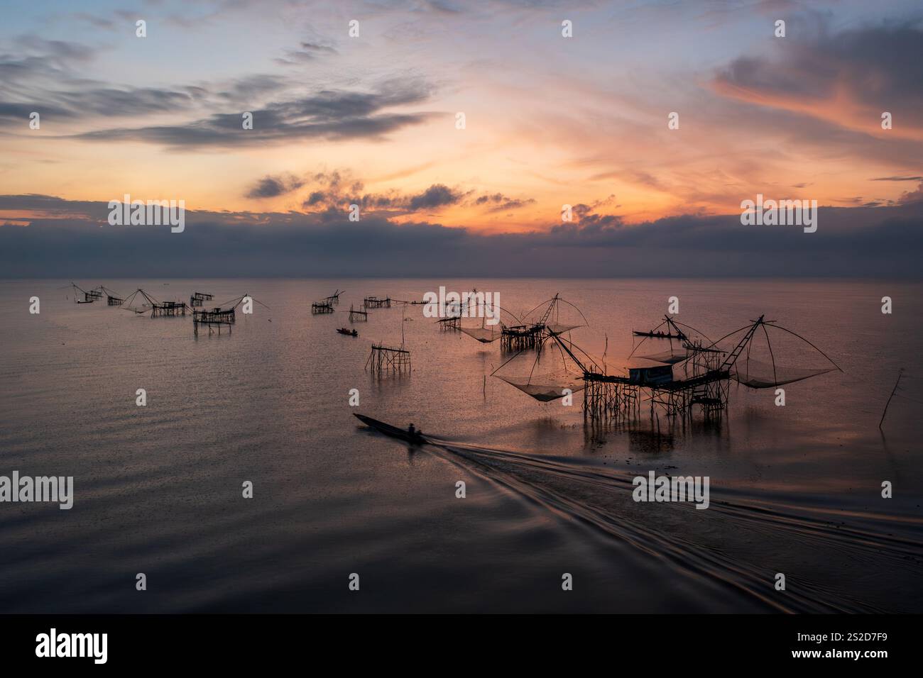 Sagoma di una barca che naviga accanto alle tradizionali reti da pesca e piattaforme sul fiume Pak Pra all'alba, Phatthalung, Thailandia Foto Stock