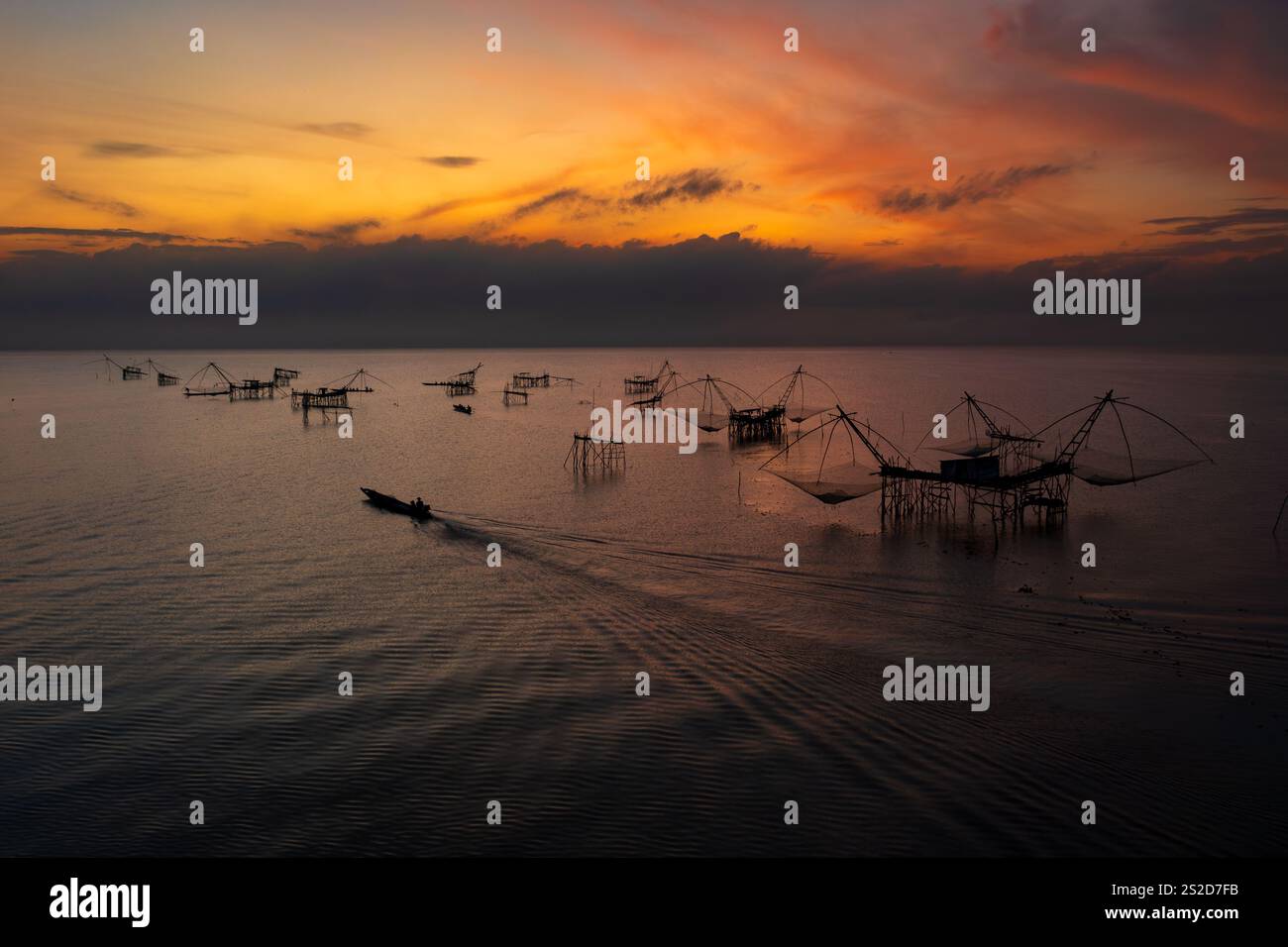 Sagoma di una barca che naviga accanto alle tradizionali reti da pesca e piattaforme sul fiume Pak Pra all'alba, Phatthalung, Thailandia Foto Stock