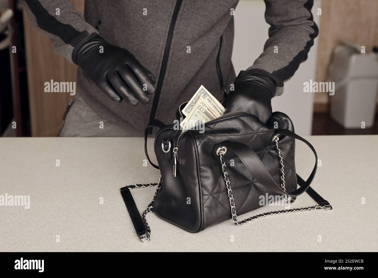 Ladro in abito nero e guanti vedere in aperto rubato donna borsa. Il ladro prende fuori le fatture del dollaro US da una borsa del womans nell'interno della cucina Foto Stock