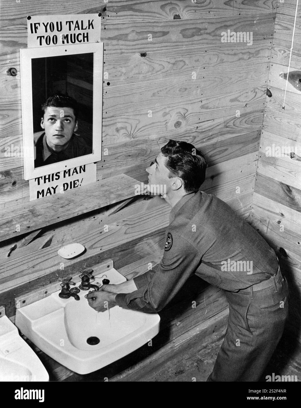 Un soldato americano guarda nello specchio del bagno con un cartello che dice "SE PARLI TROPPO QUEST'UOMO POTREBBE MORIRE!". Incoraggiamento a non diffondere informazioni che potrebbero essere sensibili nello sforzo bellico durante la seconda guerra mondiale Camp Hood, Texas, 1943 Foto Stock