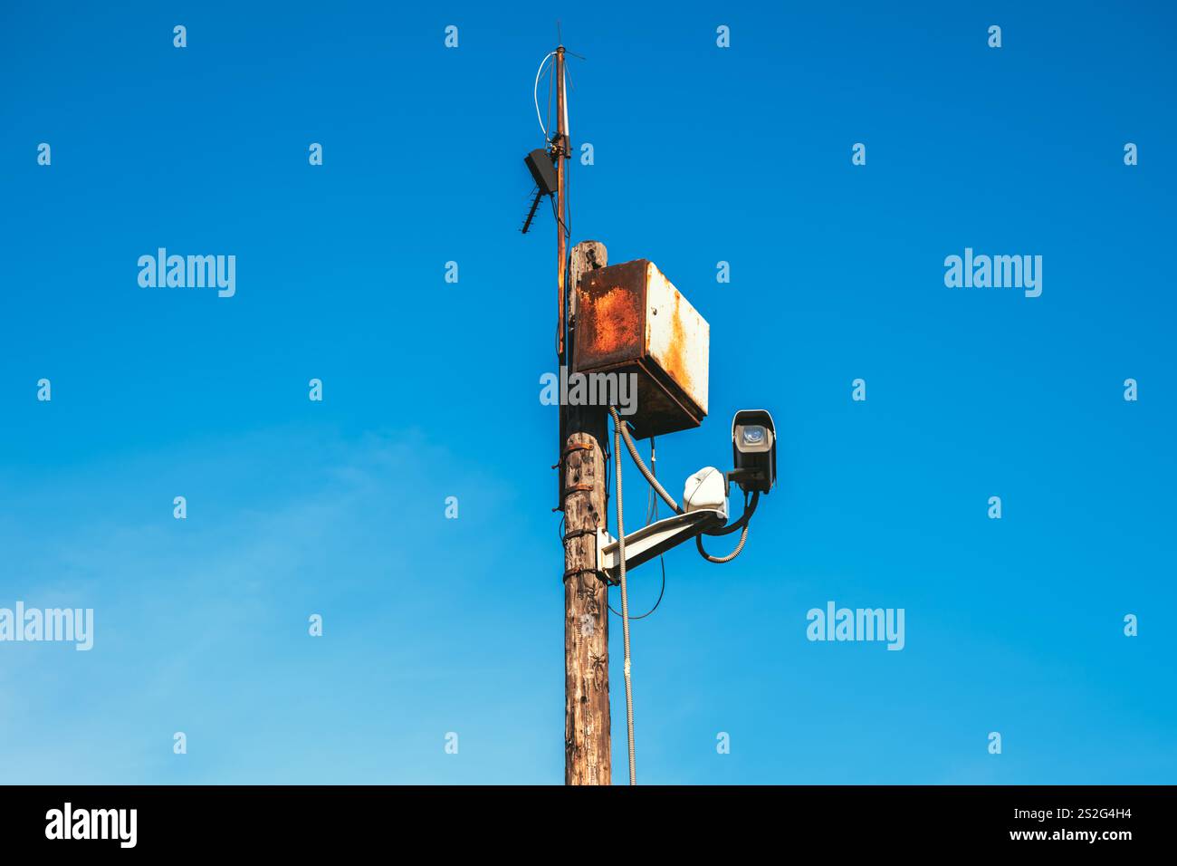 Telecamera di sorveglianza e scatola di controllo corrosa e arrugginita su palo in legno sulla strada, messa a fuoco selettiva Foto Stock