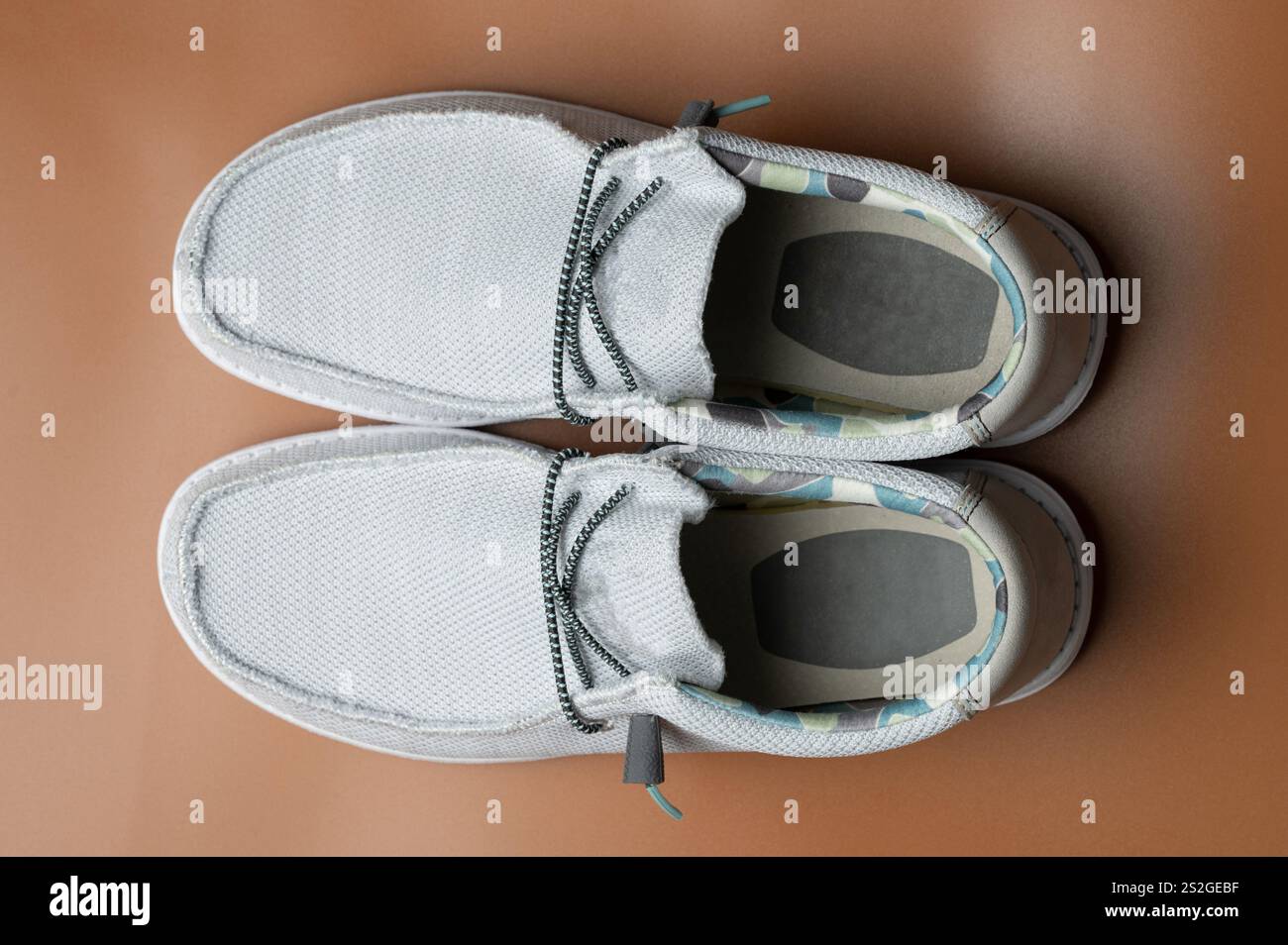 Un paio di scarpe casual bianche dal design distintivo si appoggia su una superficie liscia in legno e presenta dettagli eleganti. Foto Stock