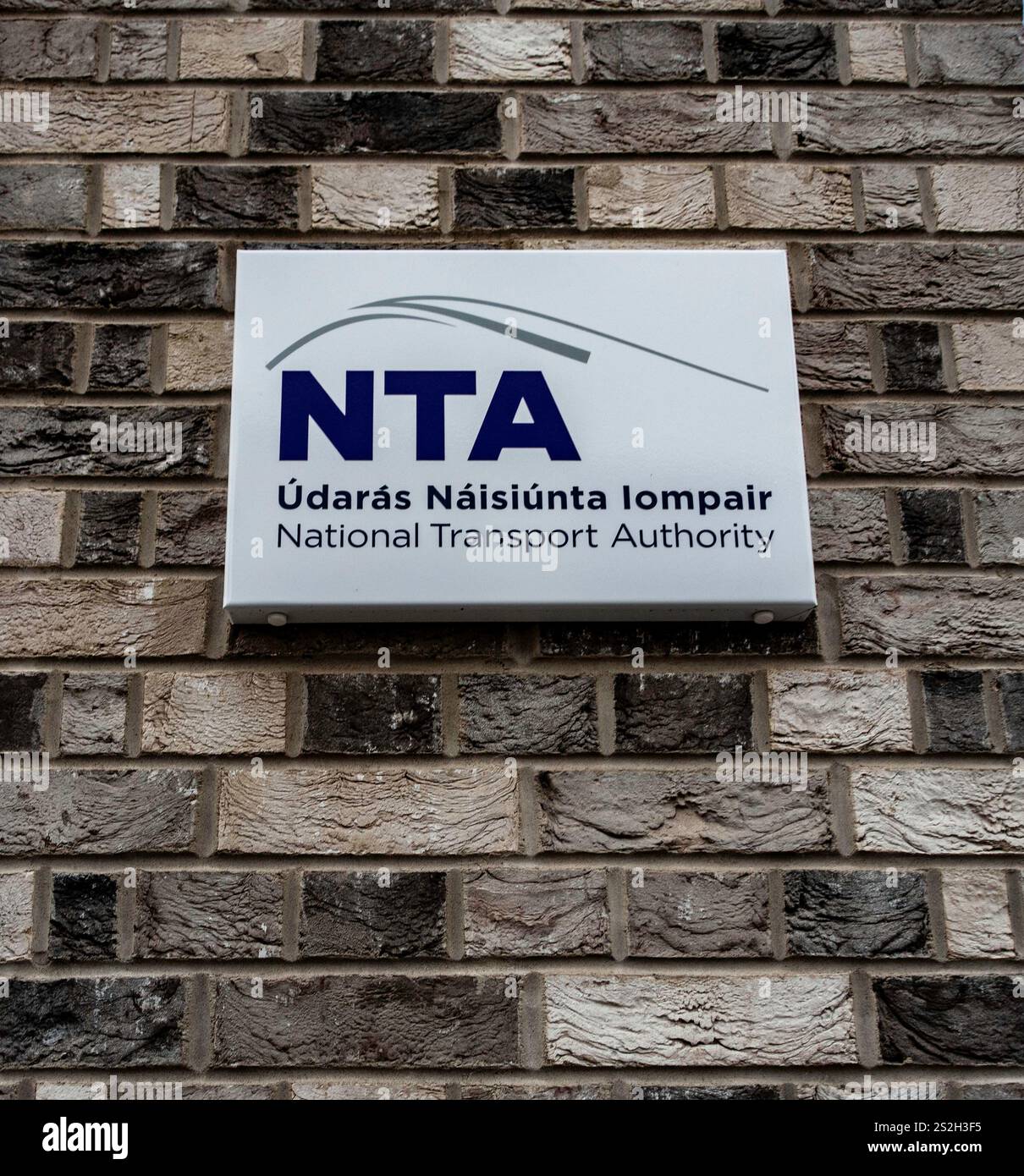 Cartello per la National Transport Authority (NTA) di Smithfield, Dublino, montato su una parete di mattoni, con testo irlandese e inglese e un logo stradale stilizzato. Foto Stock