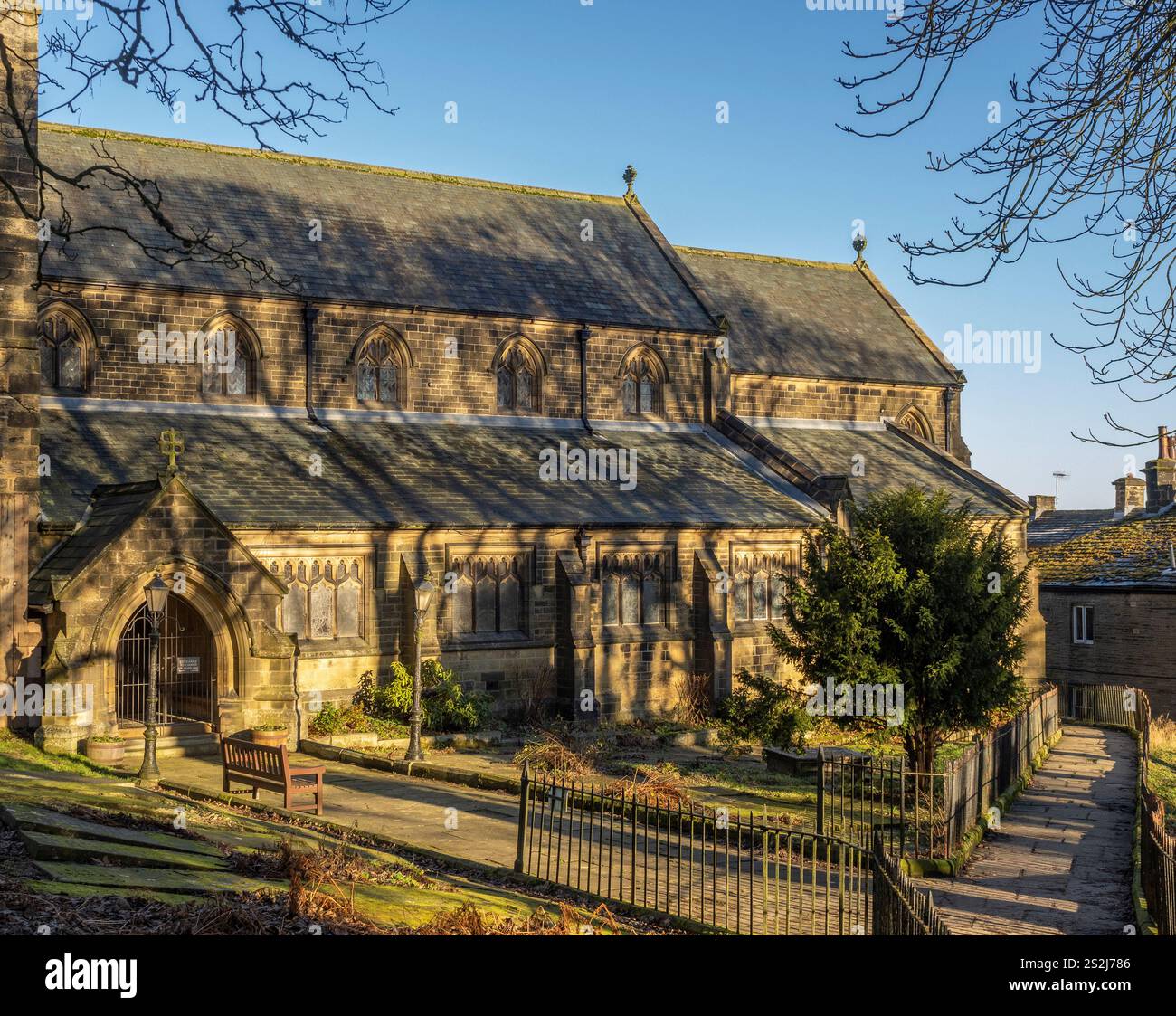 Chiesa di San Michele tutti gli Angeli a Haworth, vista dal cimitero incorniciata contro un cielo blu in una soleggiata giornata invernale. West Yorkshire, Regno Unito Foto Stock