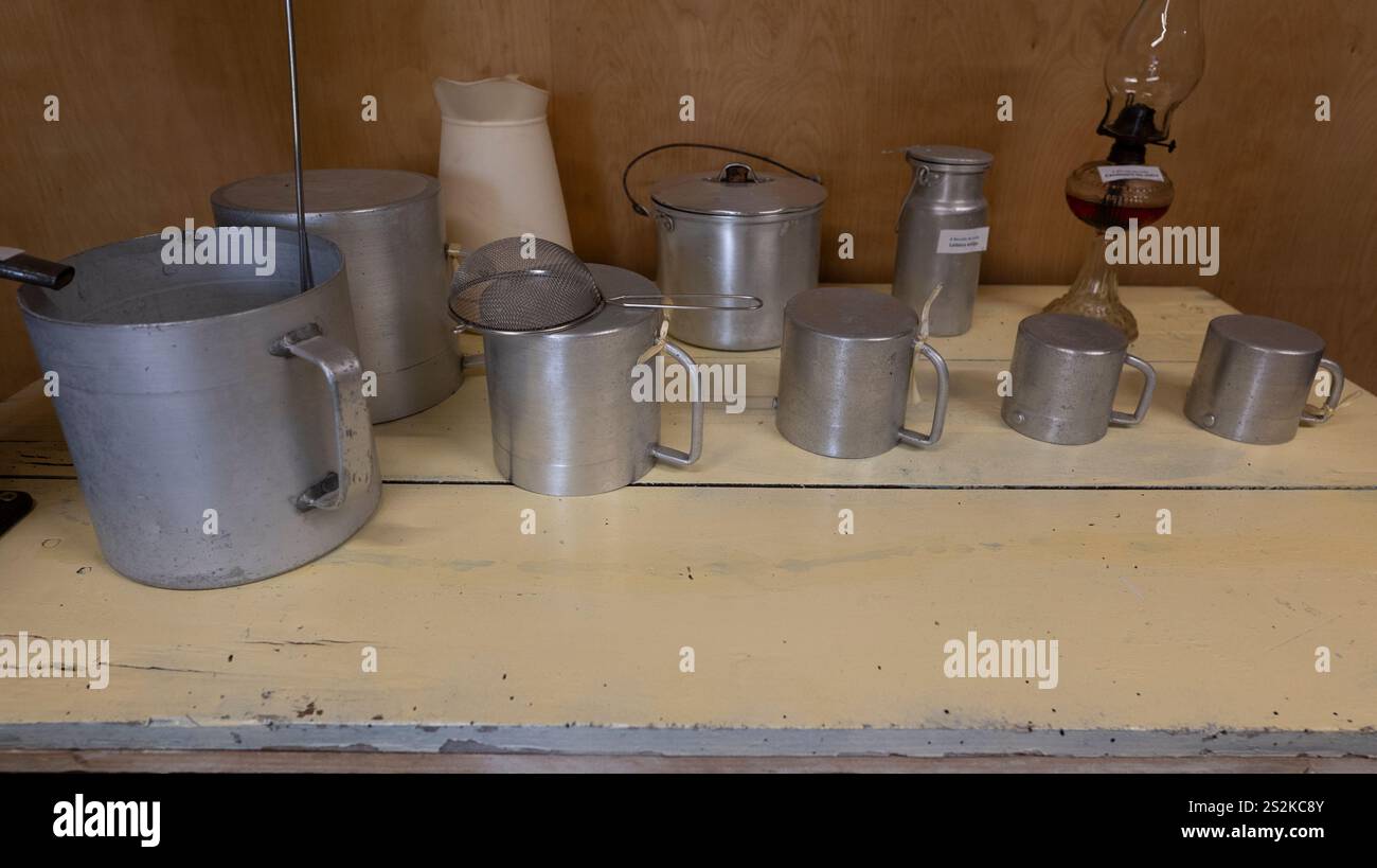 Collezione di utensili da cucina vintage in alluminio, tra cui pentole, brocche e tazze, esposti su un rustico tavolo in legno su un semplice sfondo. Foto Stock