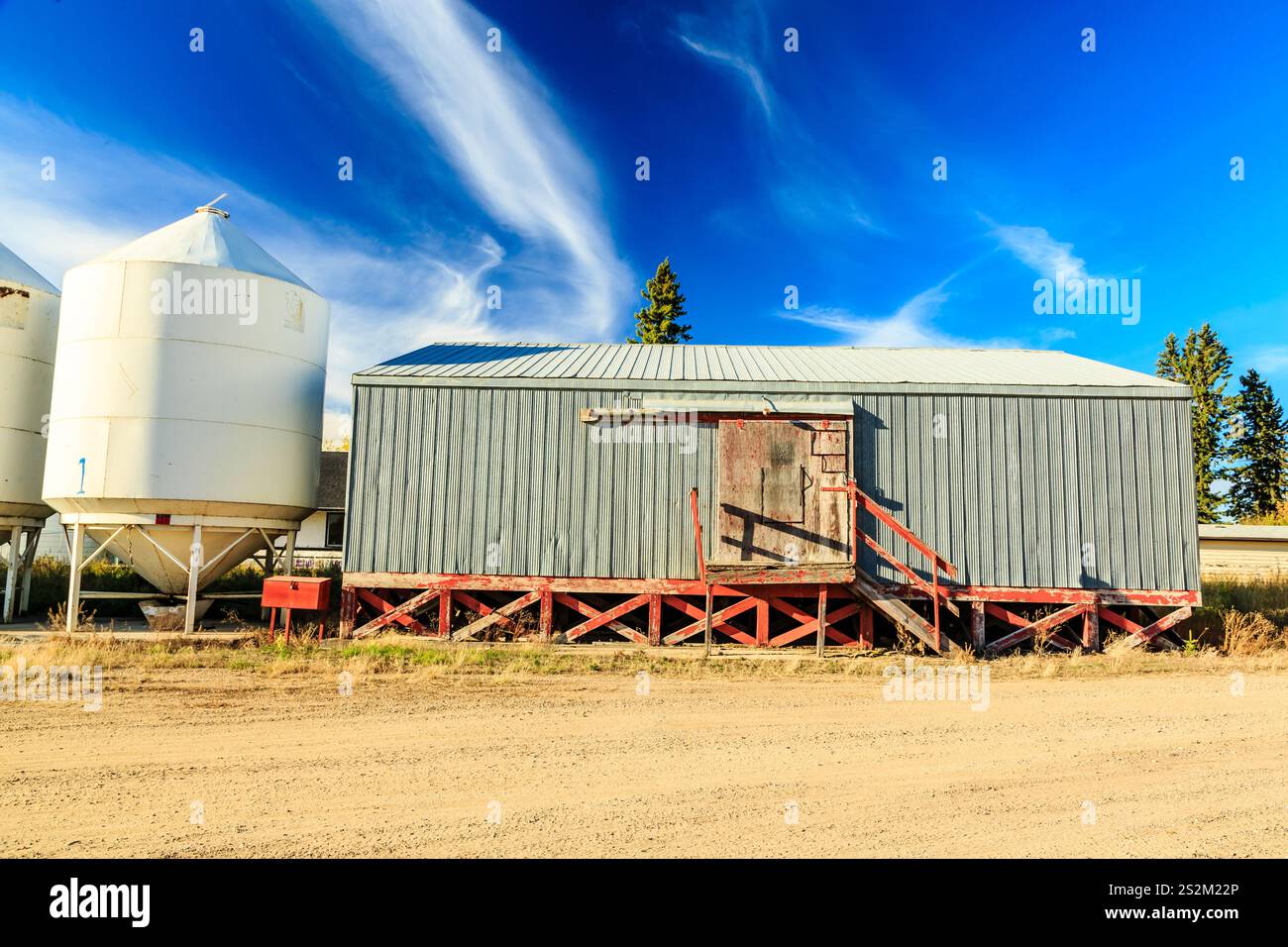 Un fienile con una porta rossa e una scala di legno. Il fienile è circondato da silos vuoti Foto Stock