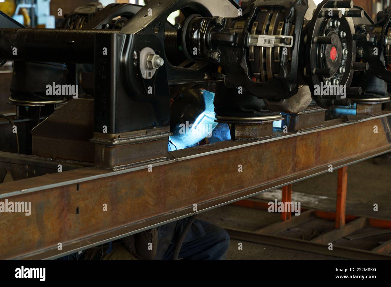 Sotto la luce fioca di un'officina, un lavoratore specializzato si concentra sulla saldatura di componenti ferroviari, scintille che volano come fusibili metallici. L'atmosfera è piena di Foto Stock