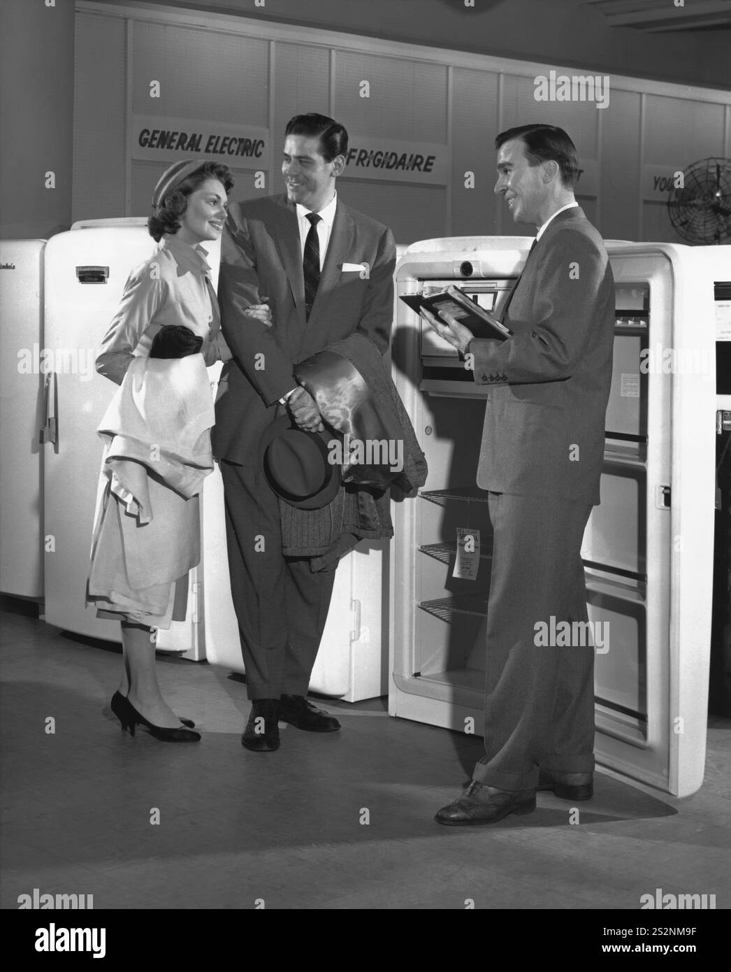Giovane coppia di mezza età ben vestita con un venditore maschile in un negozio di elettrodomestici mentre sta guardando un nuovo frigorifero Foto Stock