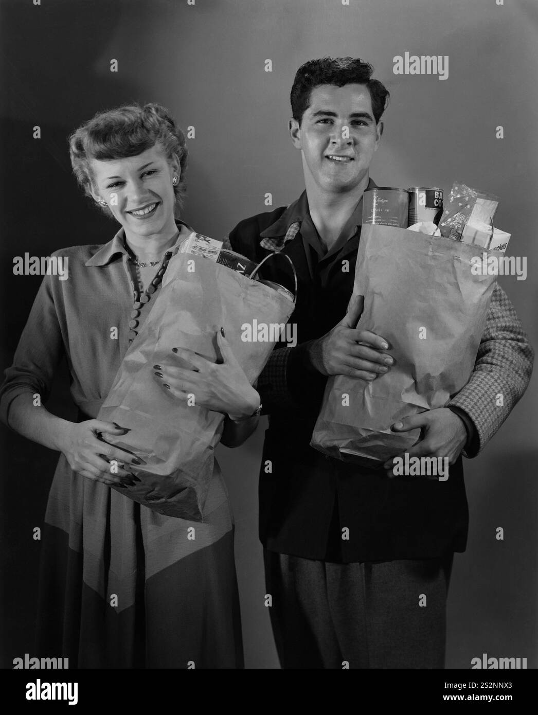 Una giovane coppia sorridente e ben vestita ha posato mentre ognuno di loro ha una borsa della spesa di carta che ha rifornito la parte superiore Foto Stock