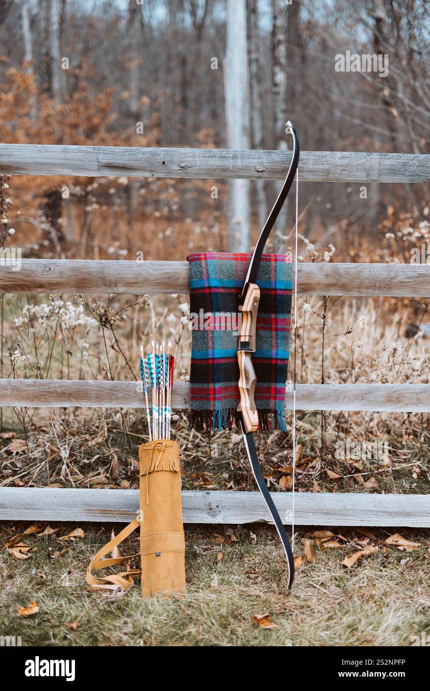 Arco di tiro con l'arco e tremola di frecce appoggiate su una coperta di lana su una recinzione a spaccatura in legno Foto Stock